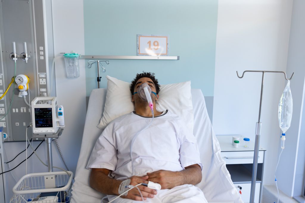 biracial male patient with oxygen mask lying bed sunny hospital room