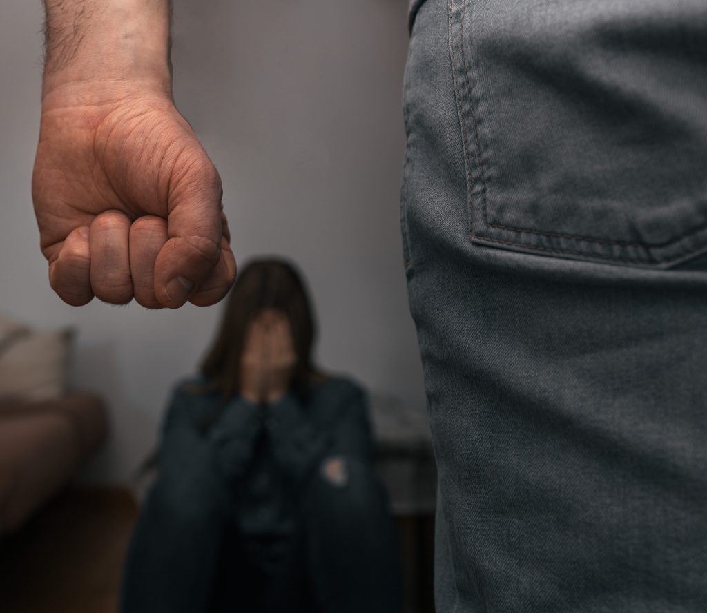man raises his fist abuse helpless woman sitting ground